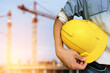 © Touch1976 - Hand's engineer worker holding yellow safety helmet with building on construction site background