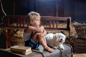 Wall Mural - Cute toddler child, blond boy, sitting on a big suitcase in the attic, with his pet dog looking sad