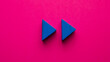 
blue wooden triangles simulating rewind symbol on pink background