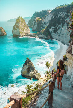 a travel girl with backpack in shorts on the ocean, cliffs and tropical beach background. nusa penid