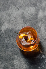 bourbon whiskey old fashioned cocktail with large ice cube and cherry orange on gold cocktail pick top shot