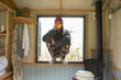 © Sam Edwards/Caia Image - Young man in pajamas drinking coffee in tiny cabin window