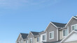 Pano Homes with gable roofs and gray exterior walls against blue sky in the suburbs