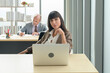 © tonefotografia - Young businesswoman sitting and working with laptop at modern office with colleague behind