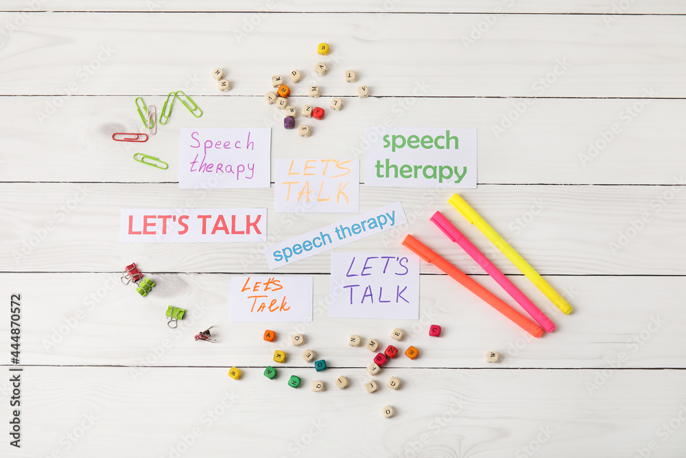 Paper pieces with text LET'S TALK and SPEECH THERAPY on white wooden background