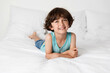 © Lisa Tichané - Smiling young boy lying on white bed resting on elbows