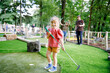 © Irina Schmidt - Cute preschool girl playing mini golf with family. Happy toddler child having fun with outdoor activity. Summer sport for children and adults, outdoors. Family vacations or resort.