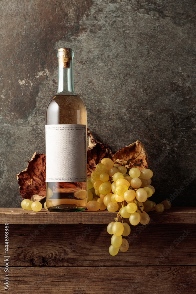 Bottle of white wine with grapes and dried up vine leaves. - obrazy, fototapety, plakaty 