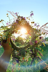 Sticker - floral wreath in hand, sunny natural background. Summer Solstice Day, Midsummer concept. floral traditional decor. pagan witch traditions, wiccan symbol and rituals