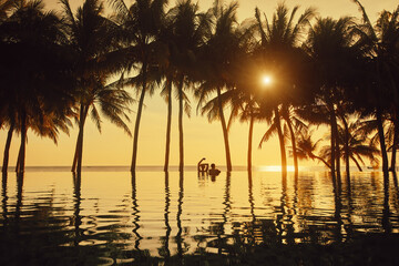 Wall Mural - Vacation Beach Summer Holiday Concept. Silhouette of happy couple relaxing in swimming pool on summer beach resort watching sunset