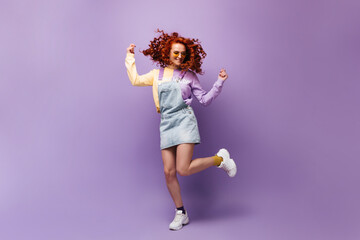 Sticker - Red-haired woman in yellow glasses having fun, jumping on lilac background