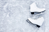White female figure skates on ice background. Sport accessories for outdoor activities in cold winter season. Closeup. Empty place for text. Top down view.
