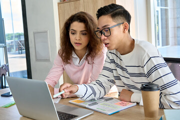 Teen latin girl and Asian guy students talking about class work using laptop computer. Multiethnic classmates discussing smart solutions startup business project. Cooperation teamwork concept.