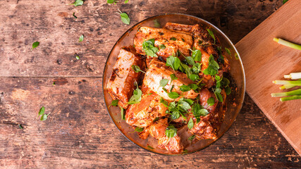 Cooking pork ribs - raw chopped pork ribs marinated in a hot sauce with fresh basil in a bowl on the table, top view, copy space