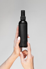 A black bottle of cosmetic spray with an empty label in a woman's hand on a light background