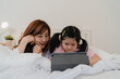© tirachard - Asian grandmother using tablet read fairy tales to granddaughter at home. Senior Chinese, grandma happy relax with young girl before bedtime lying on bed in bedroom at home at night concept.