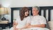 © tirachard - Asian senior couple talking on bed at home. Asian Senior Chinese grandparents, husband and wife happy relax together after wake up while lying on bed in bedroom at home in the morning concept.