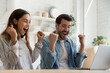 © fizkes - Overjoyed mixed race couple sit in kitchen looking at laptop screen celebrate online lottery victory. Happy young spouses read great news feeling amazed scream with joy enjoy big sale discount concept