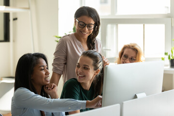 Canvas Print - Happy diverse female business team meeting at desktop computer, watching presentation on monitor, talking about work tasks, smiling, laughing. Employee presenting project solution, showing content