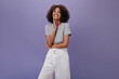 © Look! - Girl in gray t-shirt is smiling on isolated background. Cheerful curly woman in white shorts laughing on purple backdrop