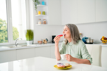 Sticker - Portrait of attractive elderly dreamy grey-haired woman drinking coffee eating yummy tasty bakery at home light white indoors