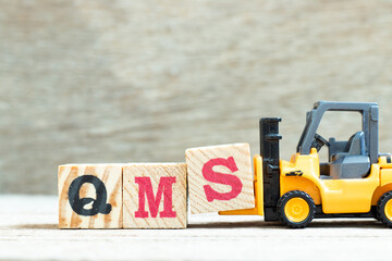 Sticker - Toy forklift hold letter block S to complete word QMS (abbreviation of quality management system) on wood background