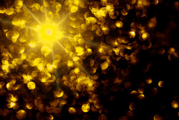 Blurred gold bokeh on black background. Golden glowing background. Abstract defocused backdrop.