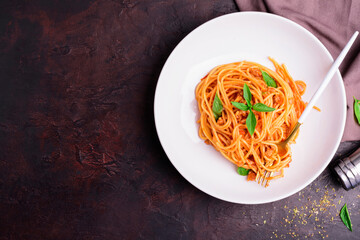 Wall Mural - Appetizing classic Italian spaghetti pasta with tomato and basil sauce and fork arranged on a white plate. On a dark wooden table - top view