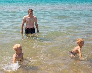 A man with his children are swimming in the sea. Boys and daddy have fun in the water