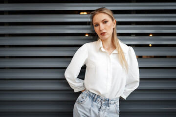 Sticker - Stylish girl in jeans and white cotton blouse posing near gray wall