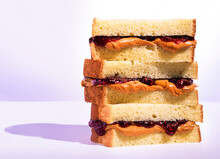 Stack Of Peanutbutter And Jelly Sandwiches With Raspberry Jam On A Light Purple Background With Dramatic Lighting & Shadows.