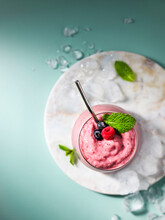 Overhead Image Of A Berry And Mint Smoothie On A Marble Tray With Ice On A Pastel Green Surface.