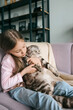 © k8most - Adorable, cute, smiling girl hugging Scottish gray cat on the sofa at home. Pets, friendship, home, happiness concept