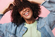 © Look! - Smiling curly woman in denim jacket posing over pink background. Joyful happy girl in green tee laughing on isolated backdrop