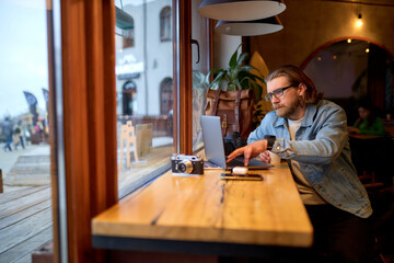 Young successful bearded man sitting at cafe and surfing internet on laptop. Concept of freelance and social networks. copy space. people lifestyle concept
