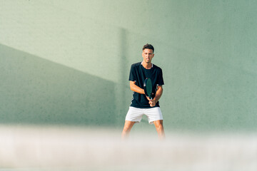 Man playing paddle tennis on an outdoor green paddle tennis court at the sunset