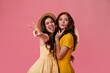 © Look! - Brunette woman shows peace sign and tongue. Girls with wavy dark hair and bright lips posing on pink background in yellow dresses
