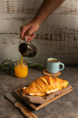 Canvas Print - Crunchy delicious croissant with ham and cheese filling, a mug of hot coffee and juice on a table