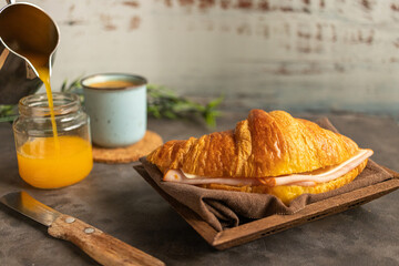 Sticker - Crunchy delicious croissant with ham and cheese filling, a mug of hot coffee and juice on a table