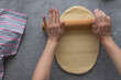 Dough flatten by white blurred woman hands using a rolling pin on a rustic gray table.