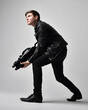 Full length portrait of a  brunette man wearing leather jacket  and holding a science fiction gun.  Standing  action pose isolated  against a grey studio background.