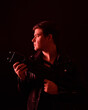 © faestock - close up portrait of a  brunette man wearing leather jacket  and holding a science fiction gun.  Standing  action pose with red silhouetted lighting against a black studio background.
