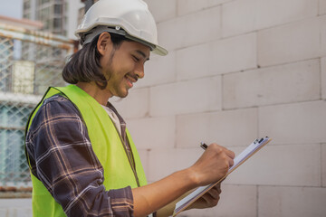 Builder, worker asian young contractor,builder man holding clipboard to plan ang wearing helmet for safety, inspect the reconstructed to construction and renovation home, check defect at site.