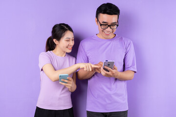 Wall Mural - Young Asian couple using smartphone on purple background
