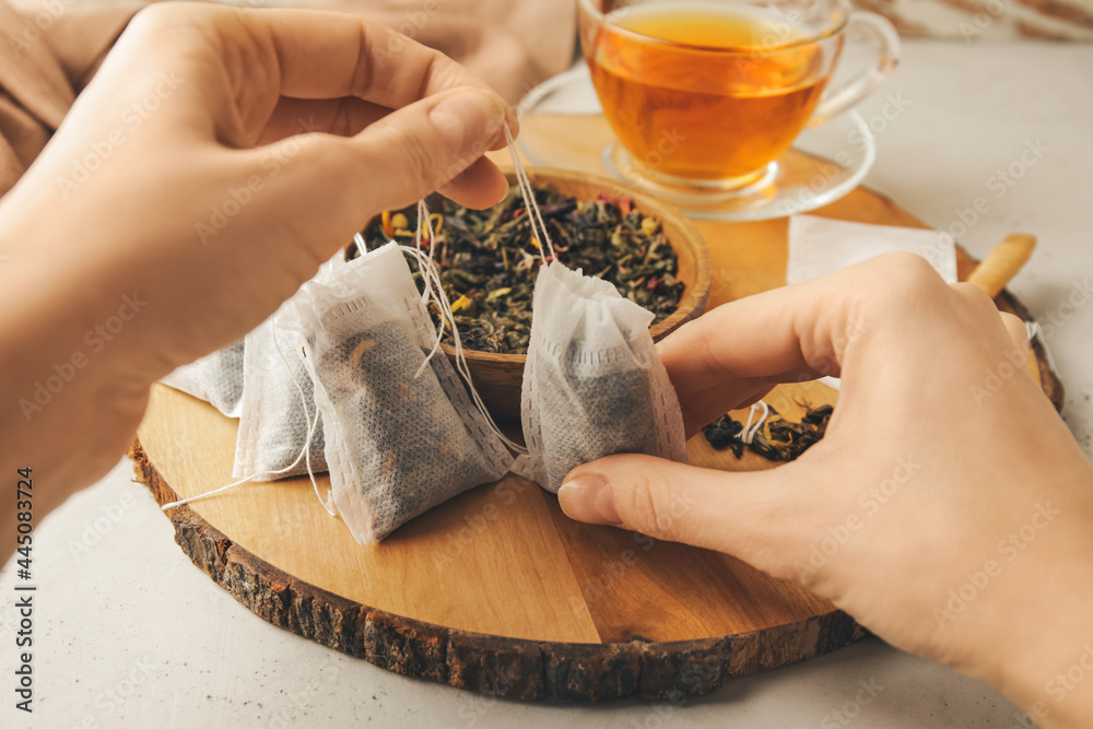 Woman with tea bags and dry leaves on light background - obrazy, fototapety, plakaty 