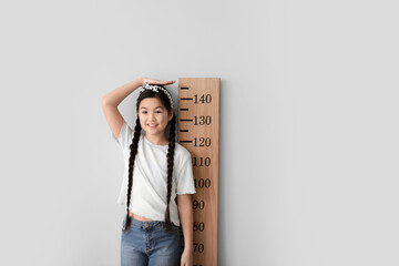 Wall Mural - Little girl measuring height near light wall