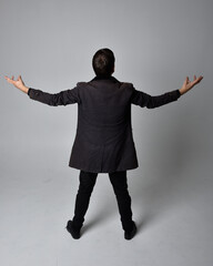 Wall Mural - Full length portrait of a brunette man wearing black leather coat.  Standing pose facing backwards, walking away from the camera isolated  against a grey studio background.