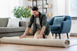 household, home improvement and interior concept - happy smiling young man unfolding carpet