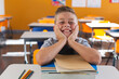 Happy caucasian schoolboy sitting at desk in classroom leaning on books and smiling