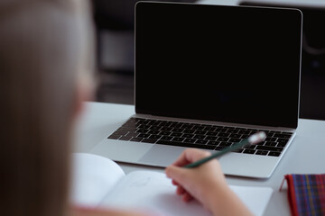 Wall Mural - Caucasian schoolgirl at desk in classroom writing and using laptop, with copy space on screen